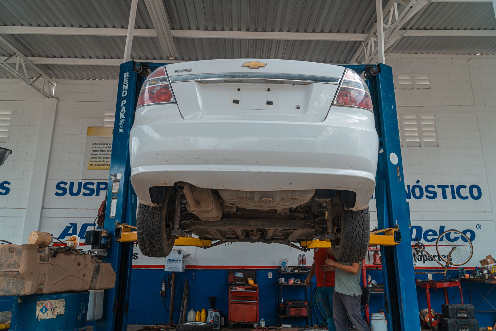 Um carro Chevrolet branco é levantado para manutenção em uma oficina automotiva.
