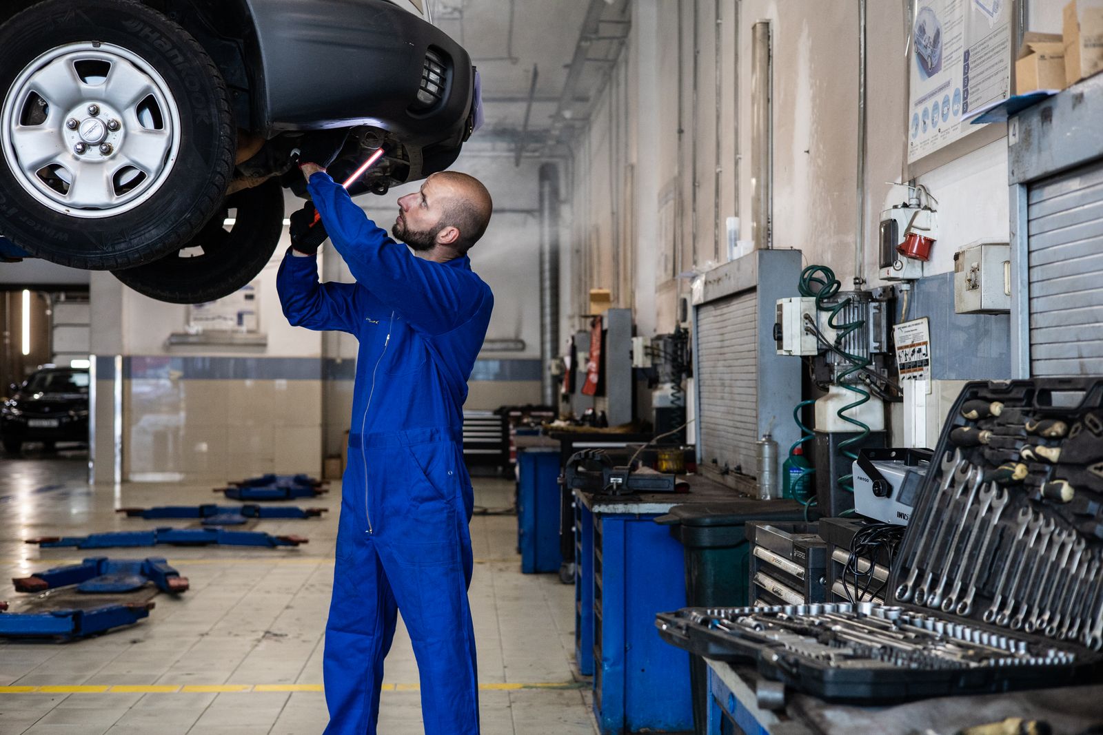 Mecânico inspecionando um carro levantado em uma oficina para serviços de manutenção e reparo.